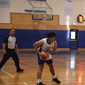 Carrie Best Scholar Caleb Rennie on the basketball court, holding a ball, with referee behind watching the play