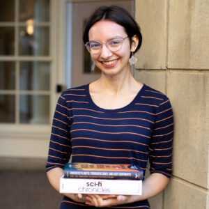 Emma Martel leaning against outside pillar holding books