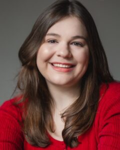 Gaby smiling to camera with long, brown hair, wearing a red shirt